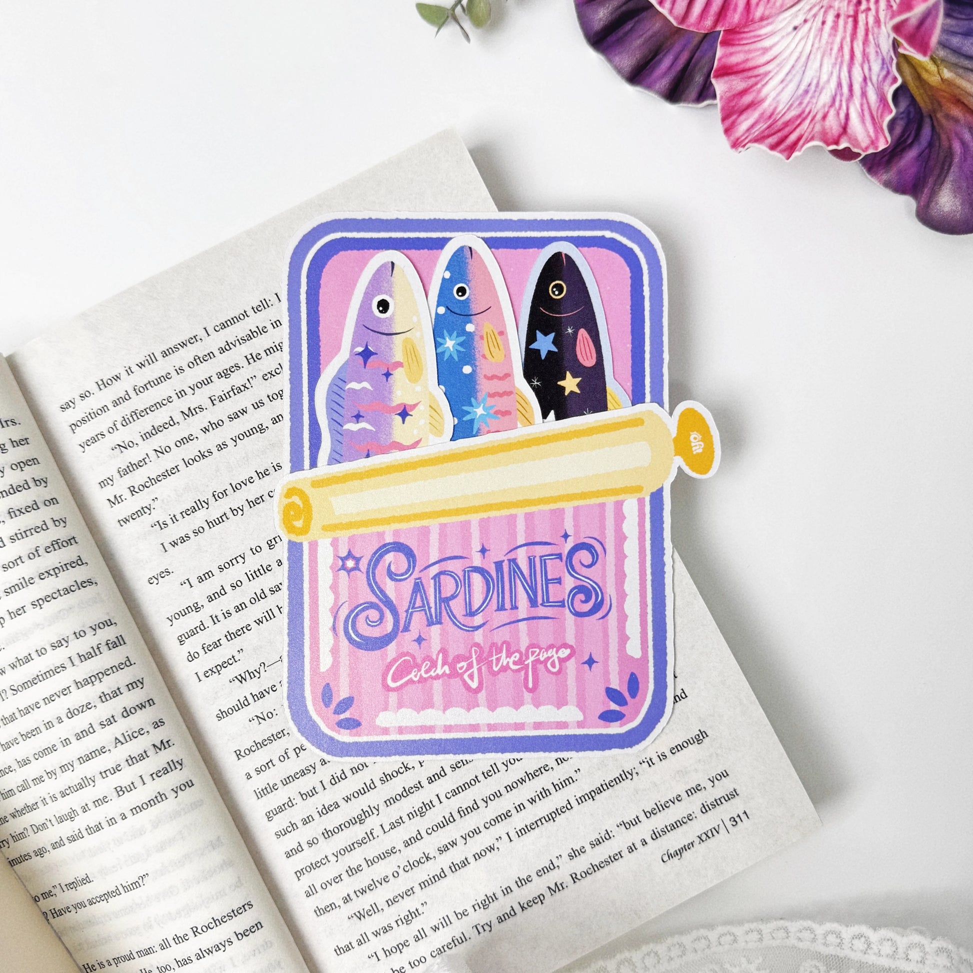 Catch of the Page Sardine Bookmark Set displayed on an open book with three fish tucked into the pink tin holder