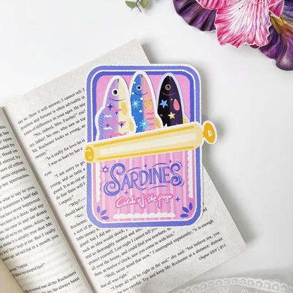 Catch of the Page Sardine Bookmark Set displayed on an open book with three fish tucked into the pink tin holder