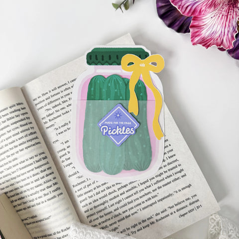 Pickle Jar Bookmark Set displayed on an open book with four green cucumber bookmarks tucked inside the pink jar holder