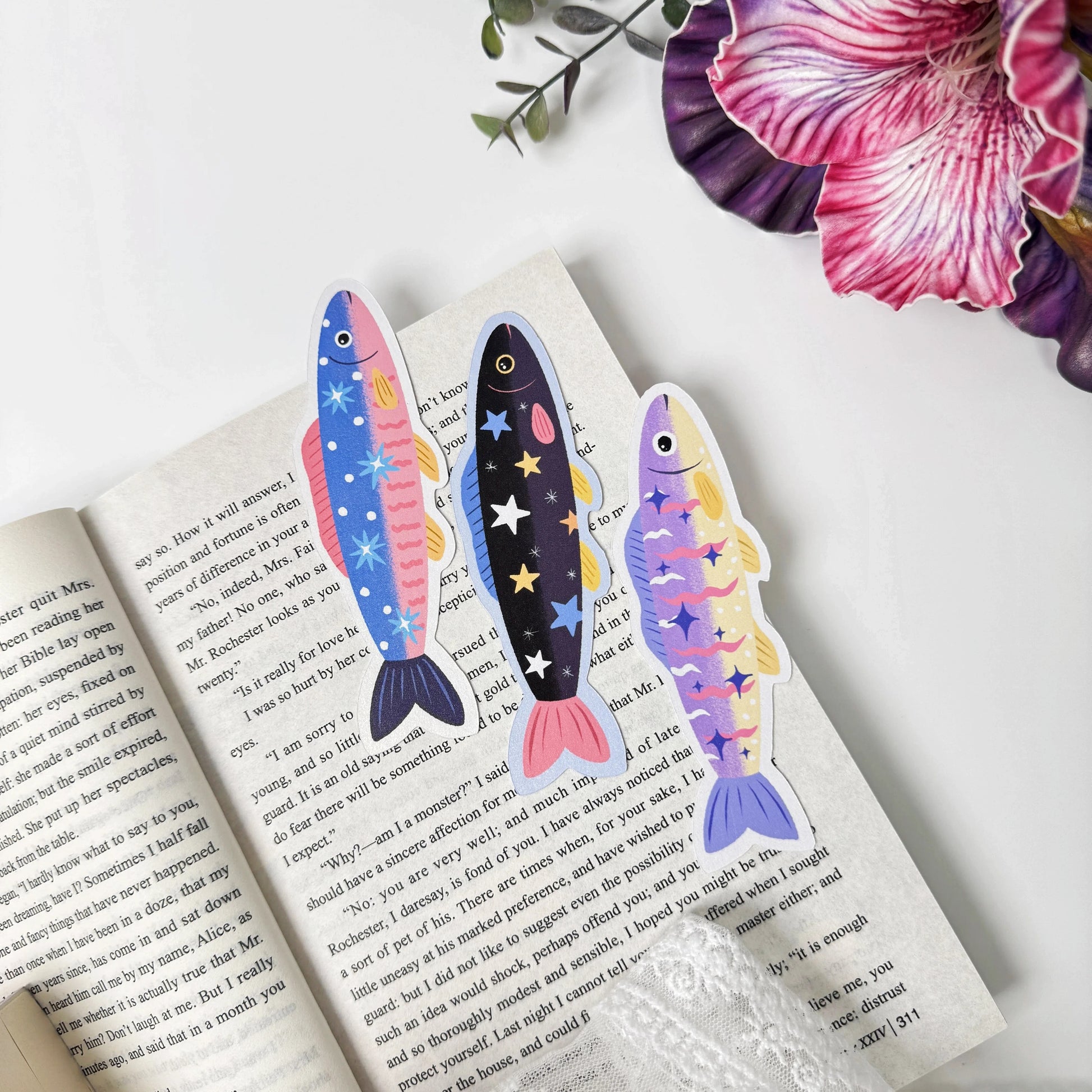 Three removable sardine bookmarks in blue, black and purple designs arranged on an open book