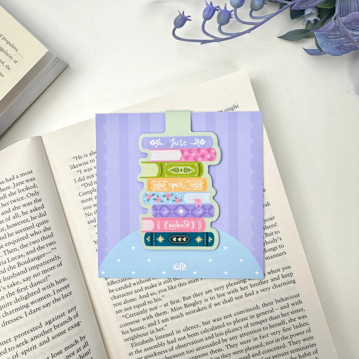 Just Keep Reading book stack magnetic bookmark on a lavender display card over an open book