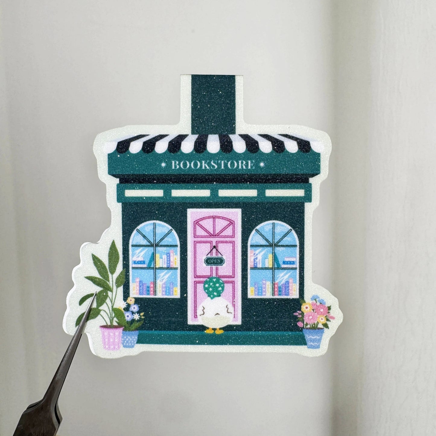 Close-up of Duck's Little Bookshop magnetic bookmark showing the green storefront, pink door and sparkling finish
