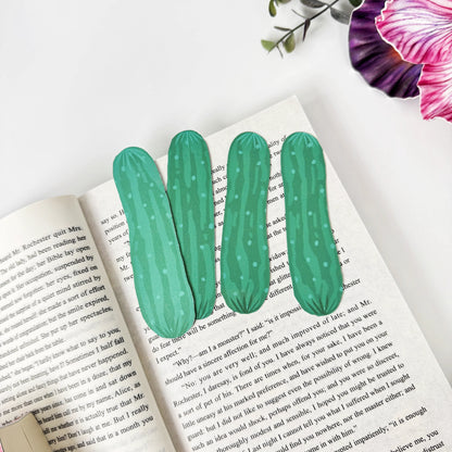 Four green cucumber bookmarks arranged across an open book beneath pink and purple flowers