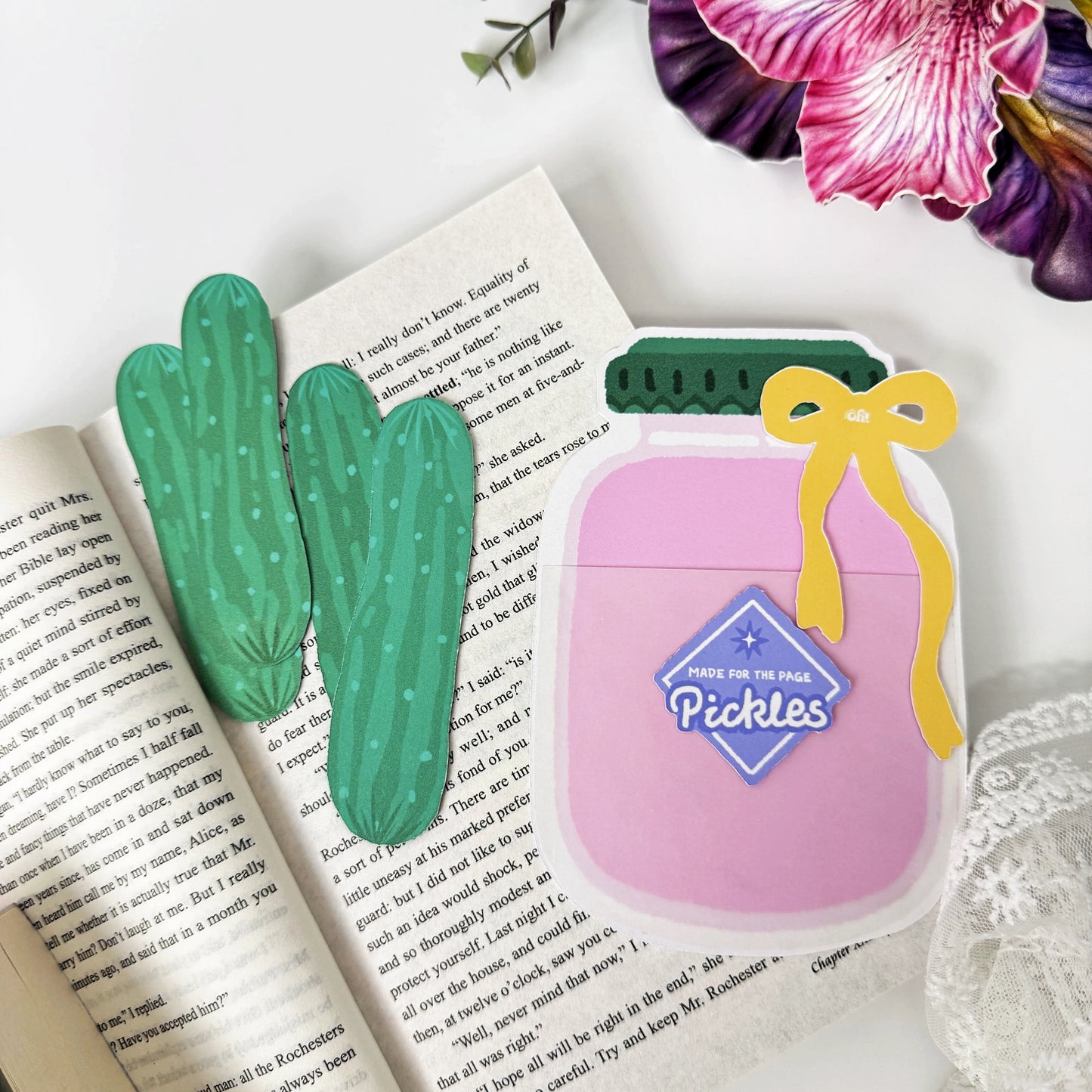 Pink Pickle Jar holder with a yellow bow beside four removable cucumber bookmarks on an open book