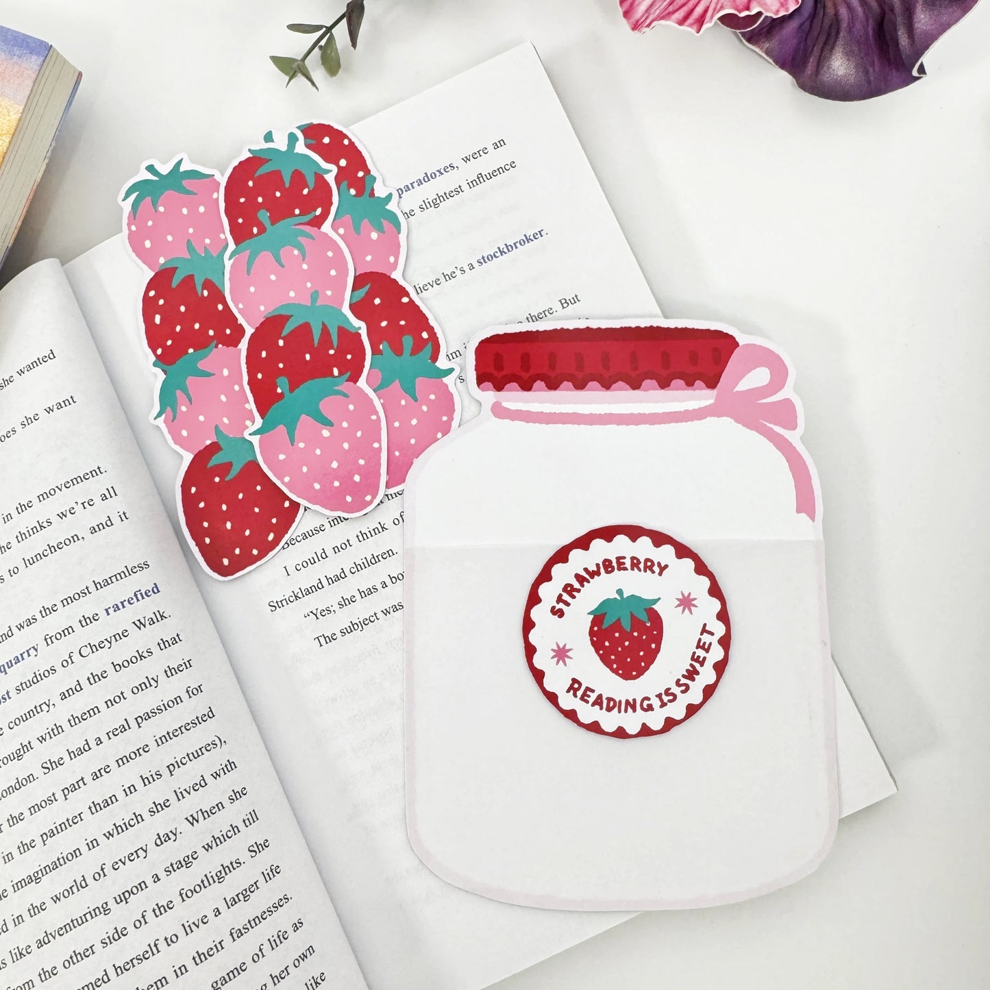 Three strawberry bookmarks removed and arranged beside the empty Strawberry Jar holder on an open book