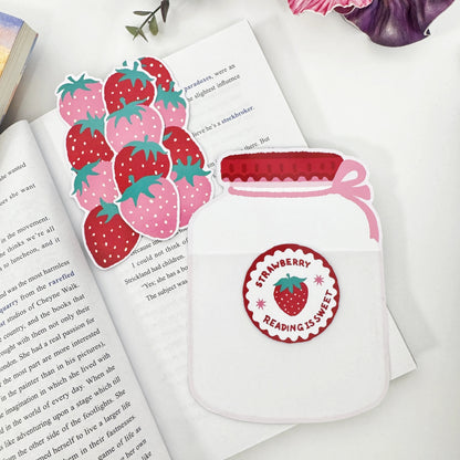 Three strawberry bookmarks removed and arranged beside the empty Strawberry Jar holder on an open book